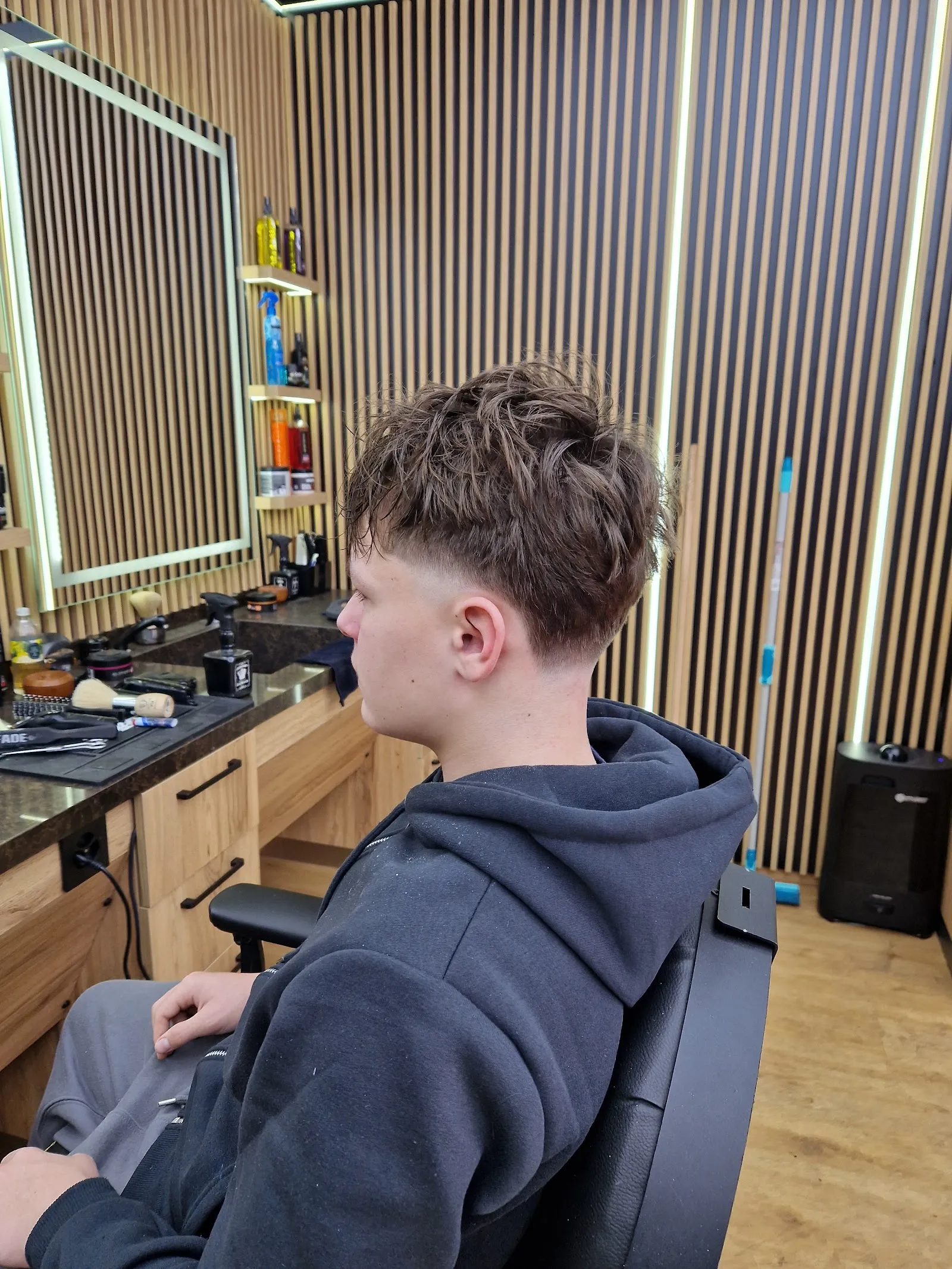 Dégradé bas frais sur cheveux mi-longs, devant les murs à lattes du salon